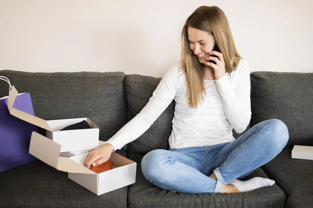 Frau sitzt auf dem Sofa und packt eine Onlinebestellung aus
