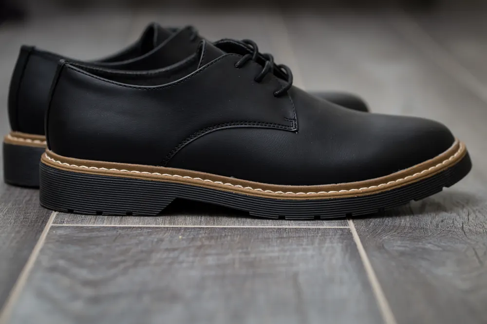 Schwarzer Herren-Schnürschuh mit umlaufender Naht auf grauem Boden