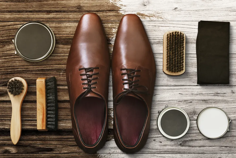 Braune Lederschuhe mit Bürsten, Creme und Poliertuch auf Holz