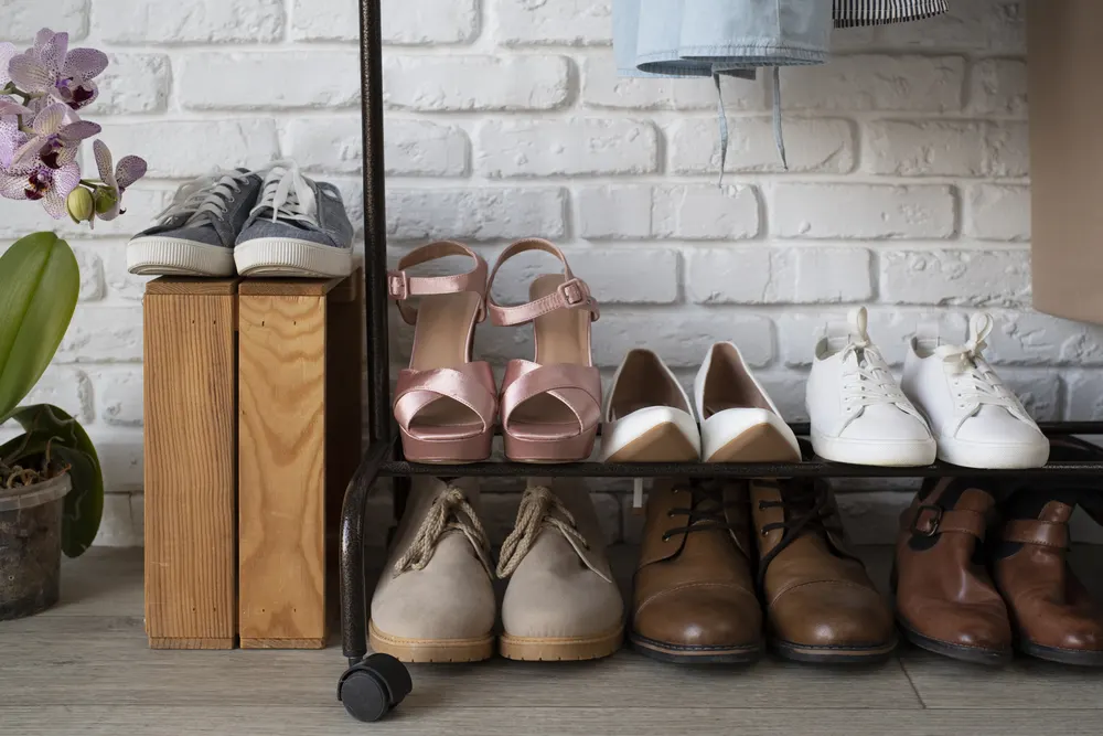 Verschiedene Schuhe auf einem Schuhregal vor einer weißen Backsteinwand