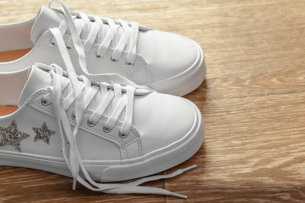 Weiße Ledersneaker mit Schnürsenkeln auf einem Holzboden